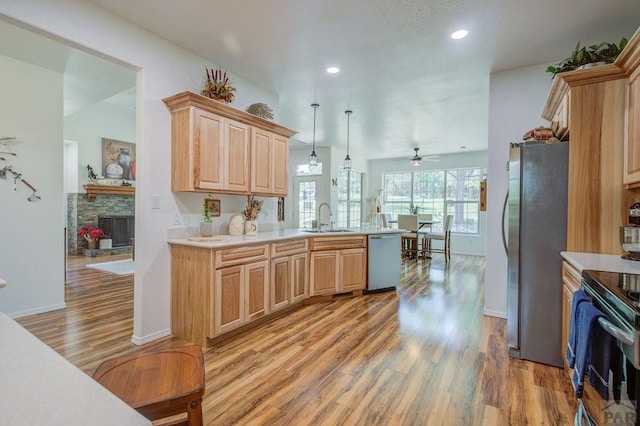 kitchen featuring a stone fireplace, light brown cabinets, stainless steel appliances, a sink, and light countertops