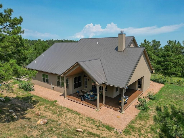 rear view of house featuring metal roof, a chimney, a wooden deck, and stucco siding