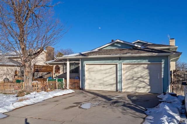 snow covered garage with fence and driveway