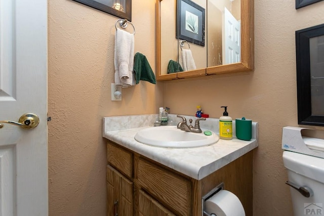 bathroom featuring toilet, a textured wall, and vanity