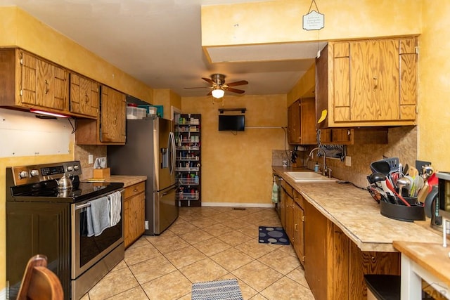 kitchen with brown cabinets, stainless steel appliances, light countertops, a sink, and light tile patterned flooring