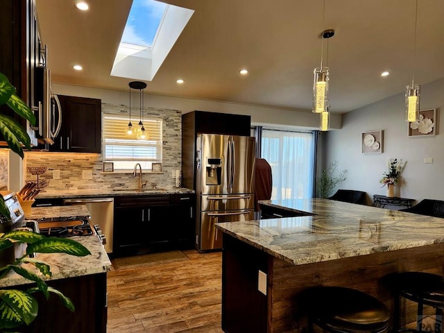 1044 S Los Charros Dr, Pueblo West, CO 81007 - kitchen with light wood-type flooring, a sink, a kitchen breakfast bar, tasteful backsplash, and appliances with stainless steel finishes
