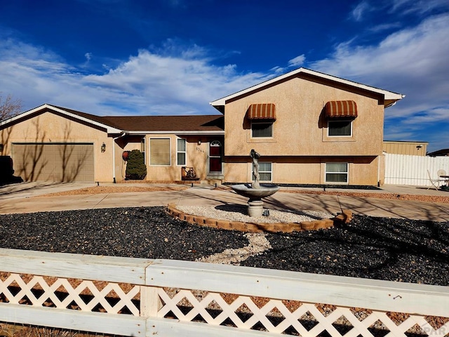 tri-level home with an attached garage, fence, and stucco siding