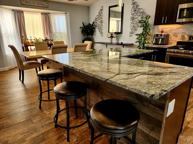 1044 S Los Charros Dr, Pueblo West, CO 81007 - kitchen featuring backsplash, a kitchen island, appliances with stainless steel finishes, a kitchen breakfast bar, and wood finished floors