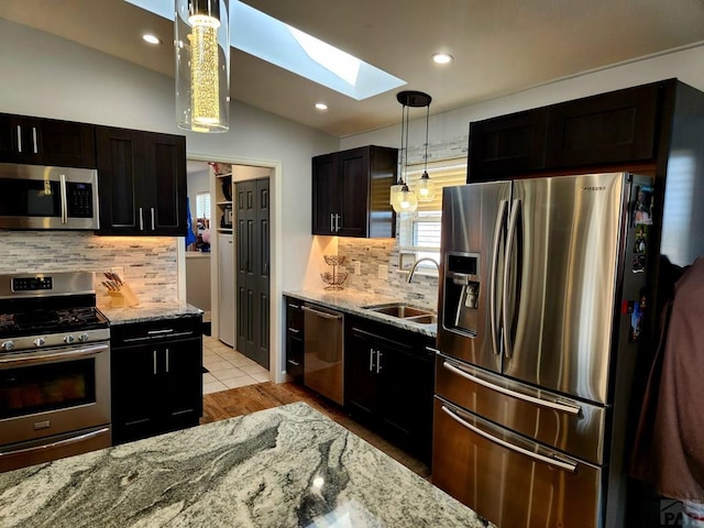 1044 S Los Charros Dr, Pueblo West, CO 81007 - kitchen featuring lofted ceiling with skylight, decorative light fixtures, light stone counters, stainless steel appliances, and a sink