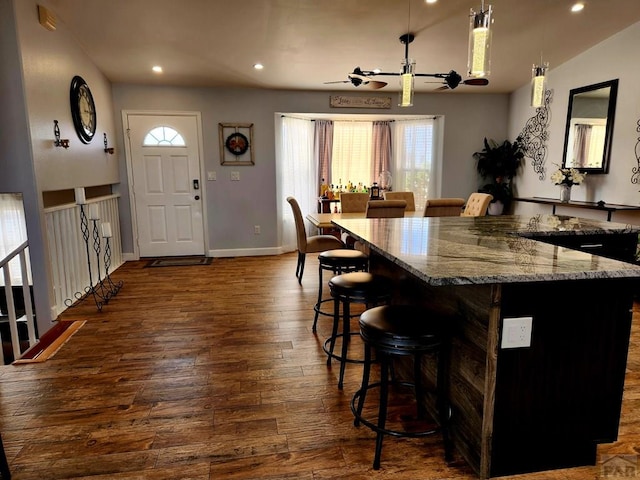 1044 S Los Charros Dr, Pueblo West, CO 81007 - kitchen featuring light stone countertops, baseboards, recessed lighting, dark wood-type flooring, and a kitchen bar
