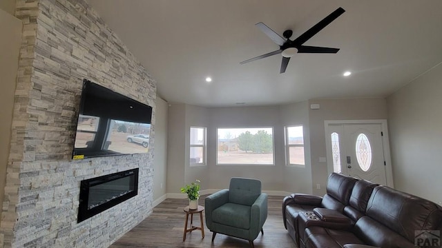 living area featuring dark wood-style floors, baseboards, a ceiling fan, recessed lighting, and a stone fireplace