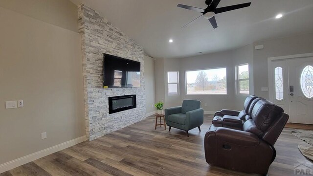 living area featuring a stone fireplace, wood finished floors, baseboards, and a wealth of natural light