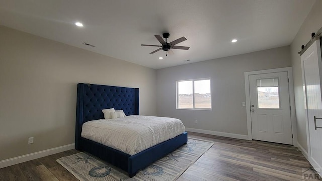 bedroom featuring a barn door, wood finished floors, baseboards, and visible vents