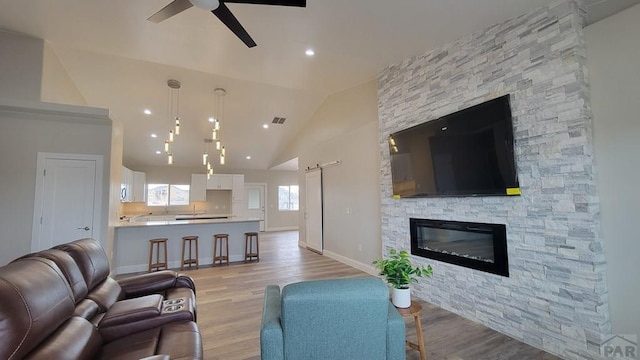 living area with a barn door, ceiling fan, vaulted ceiling, and light wood finished floors