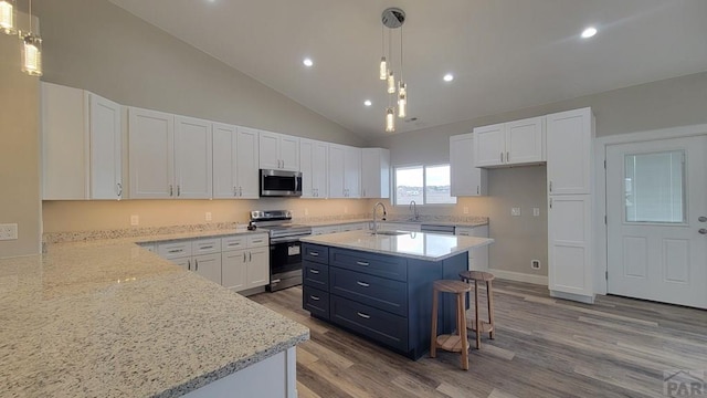 kitchen with light stone counters, wood finished floors, hanging light fixtures, appliances with stainless steel finishes, and white cabinetry