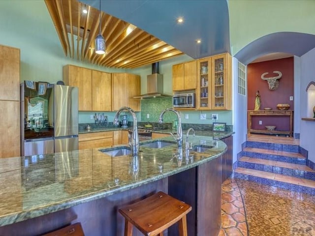 1441 Forest Rd Unit 507 1A, Creede, CO 81130 - kitchen with wall chimney range hood, stainless steel appliances, dark stone countertops, brown cabinetry, and glass insert cabinets