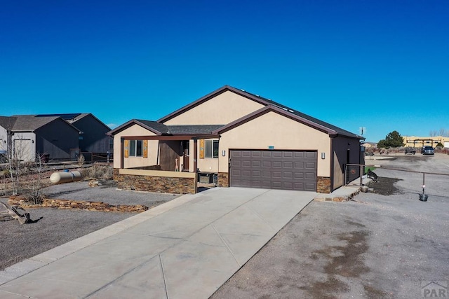 ranch-style home featuring driveway, stone siding, an attached garage, fence, and stucco siding