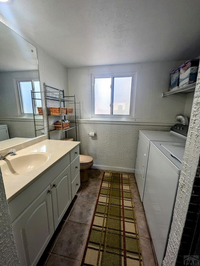 bathroom featuring a textured wall, tile patterned flooring, vanity, toilet, and washing machine and dryer