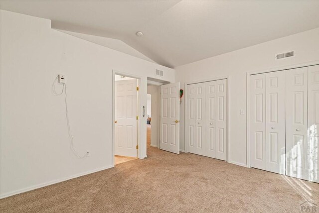 unfurnished bedroom featuring lofted ceiling, visible vents, two closets, and light colored carpet