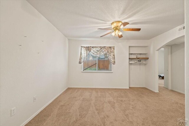 unfurnished room featuring light carpet, visible vents, arched walkways, ceiling fan, and a textured ceiling