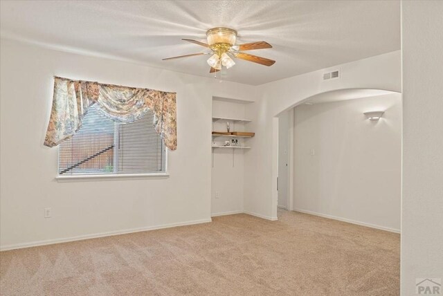 empty room featuring light colored carpet, arched walkways, visible vents, and ceiling fan