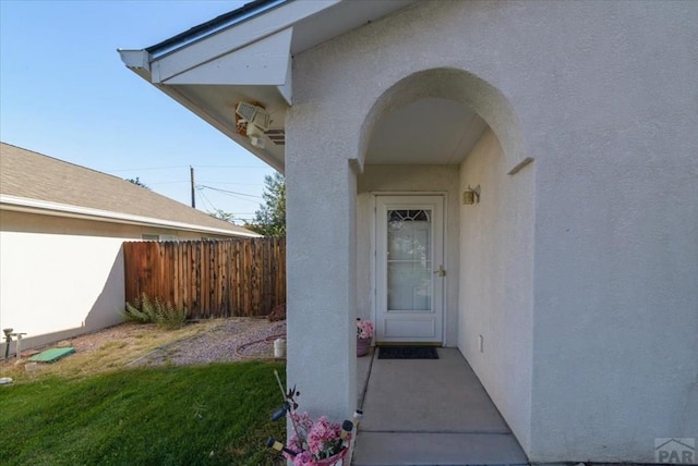 view of exterior entry with fence, a lawn, and stucco siding