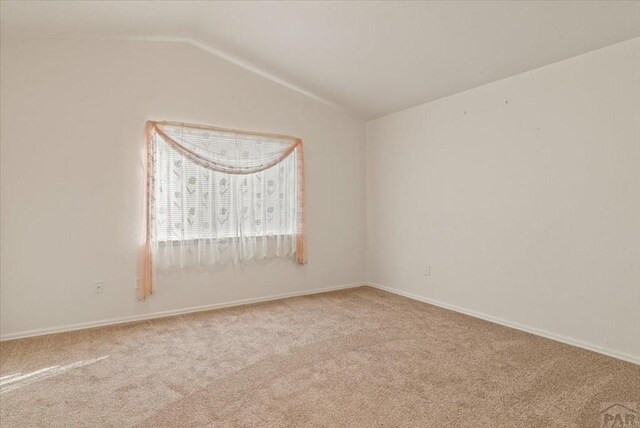 spare room with vaulted ceiling, baseboards, and light colored carpet