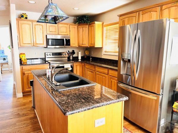 kitchen featuring an island with sink, dark stone counters, a sink, light wood finished floors, and stainless steel appliances