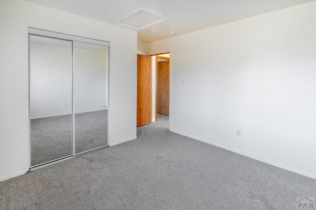 unfurnished bedroom with a closet, carpet, attic access, and baseboards