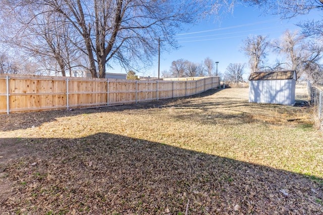 view of yard featuring a shed, a fenced backyard, and an outbuilding