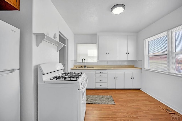 kitchen with light countertops, visible vents, white cabinetry, a sink, and white appliances