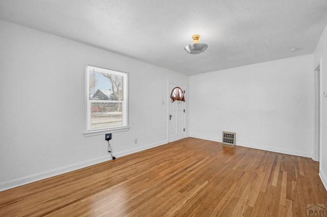 spare room featuring wood finished floors, visible vents, and baseboards