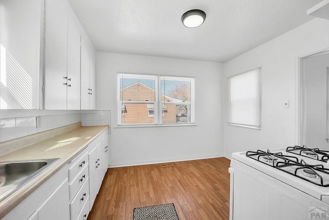 kitchen with light countertops, light wood-style flooring, white cabinetry, baseboards, and white gas range oven