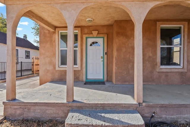 entrance to property featuring a patio area, fence, and stucco siding