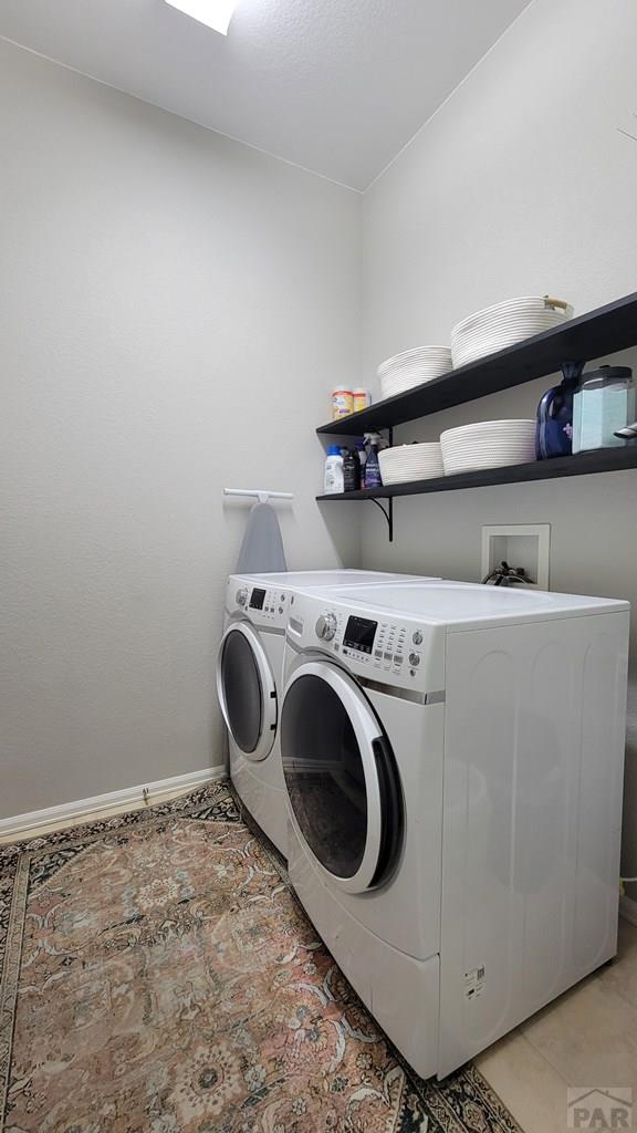 clothes washing area with light tile patterned flooring, laundry area, washing machine and dryer, and baseboards