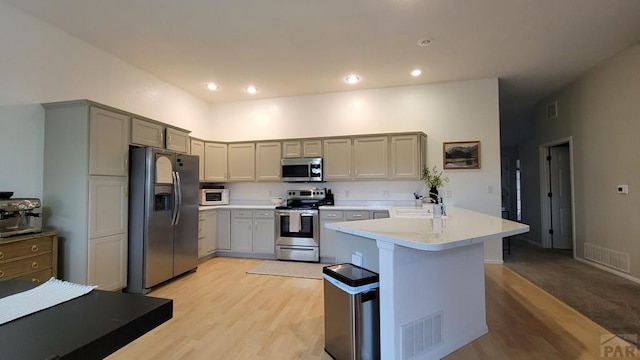 kitchen featuring visible vents, a peninsula, gray cabinets, light countertops, and appliances with stainless steel finishes