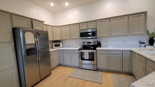 kitchen with light countertops, light wood-style floors, gray cabinets, and appliances with stainless steel finishes