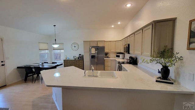 kitchen featuring a sink, stainless steel appliances, a peninsula, light wood finished floors, and light countertops