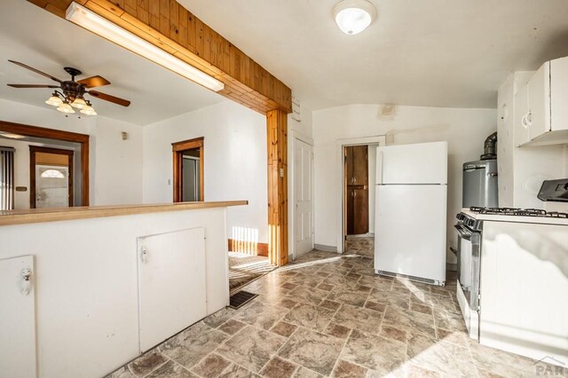 kitchen featuring stone finish flooring, ceiling fan, freestanding refrigerator, white cabinets, and gas stove