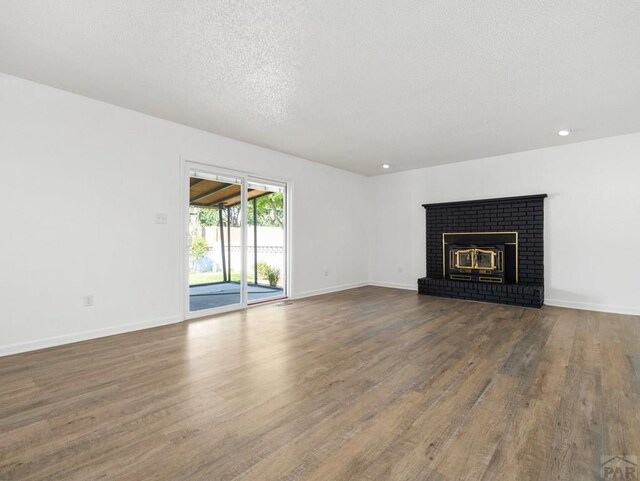 213 Starlite Dr, Pueblo, CO 81005 - unfurnished living room with wood finished floors, a textured ceiling, a brick fireplace, and recessed lighting
