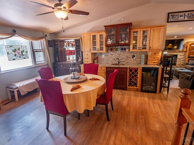 dining area featuring light wood finished floors, beverage cooler, vaulted ceiling, and indoor wet bar