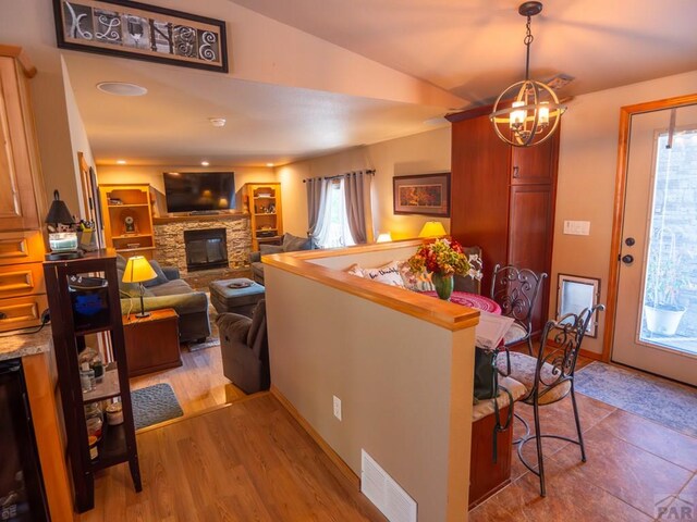 dining room featuring baseboards, visible vents, light wood-style flooring, a fireplace, and a notable chandelier