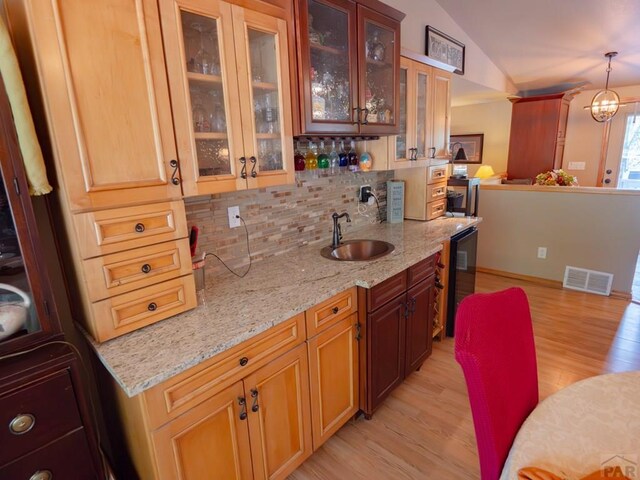 kitchen featuring visible vents, hanging light fixtures, glass insert cabinets, vaulted ceiling, and a sink