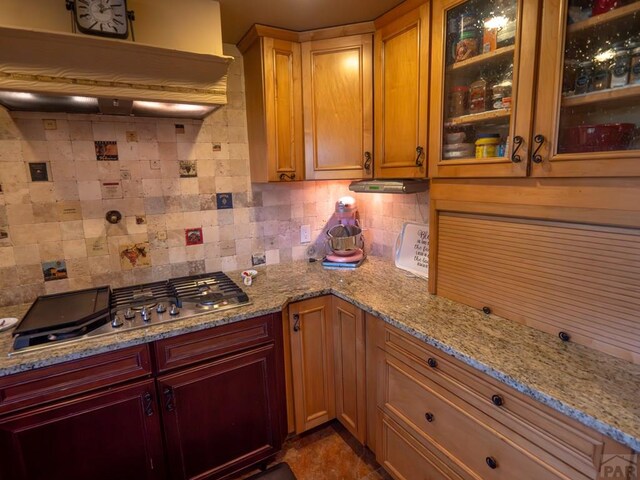 kitchen featuring stainless steel gas cooktop, backsplash, glass insert cabinets, and custom range hood