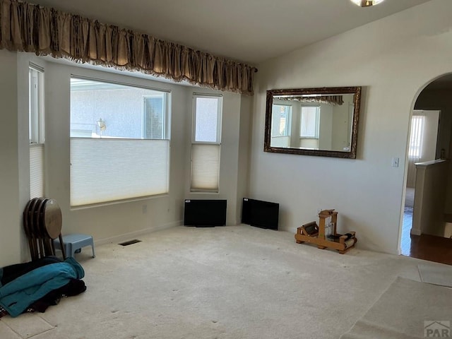 spare room with carpet floors, arched walkways, visible vents, and lofted ceiling