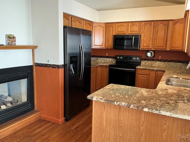 kitchen featuring light stone counters, brown cabinets, stainless steel refrigerator with ice dispenser, black range with electric stovetop, and a peninsula