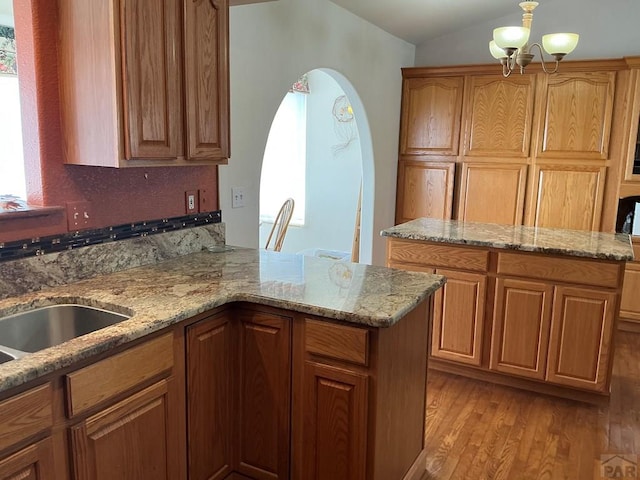 kitchen with arched walkways, hanging light fixtures, an inviting chandelier, brown cabinetry, and light wood-type flooring