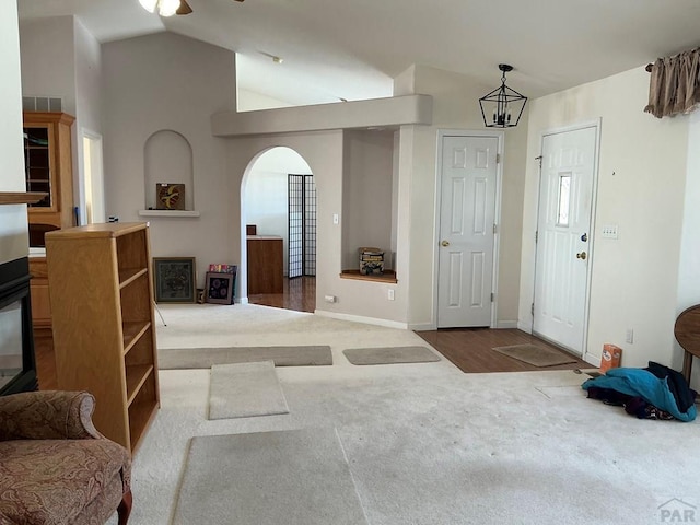 carpeted foyer featuring high vaulted ceiling, arched walkways, visible vents, and baseboards