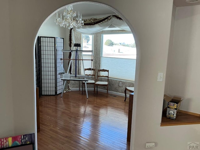 corridor featuring baseboards, arched walkways, a chandelier, and wood finished floors