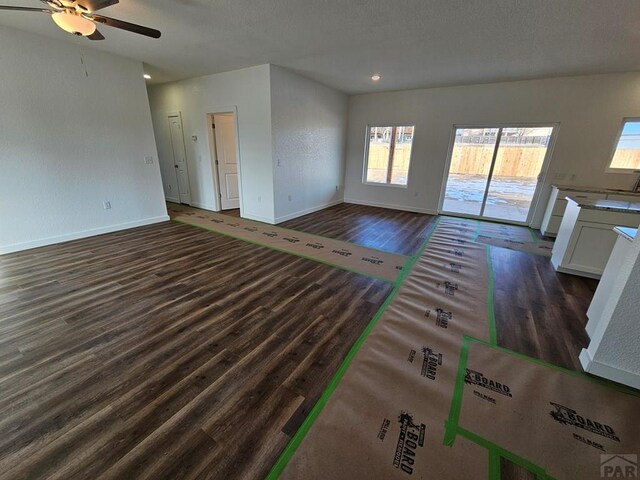 unfurnished living room with baseboards, dark wood finished floors, and a ceiling fan