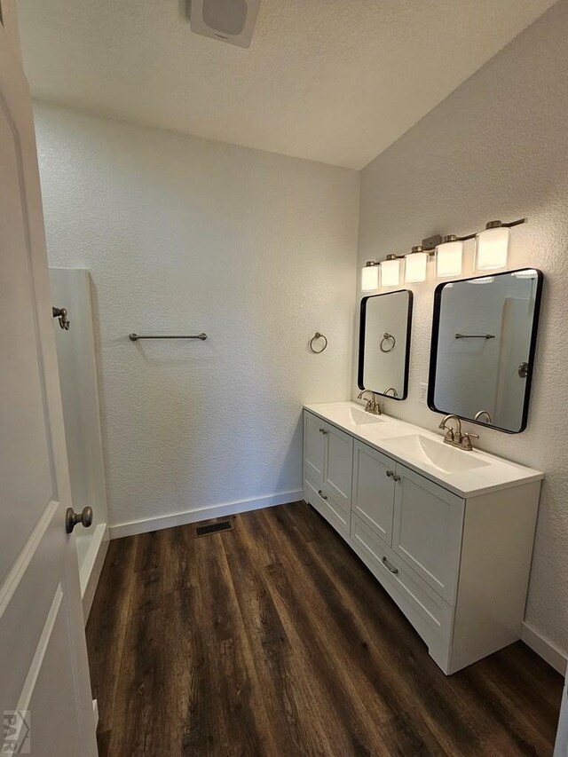 bathroom featuring double vanity, wood finished floors, a sink, and baseboards