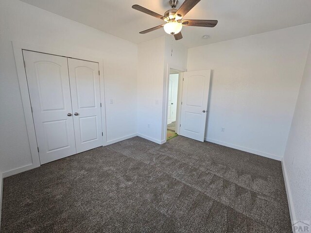 unfurnished bedroom featuring a closet, dark carpet, a ceiling fan, and baseboards