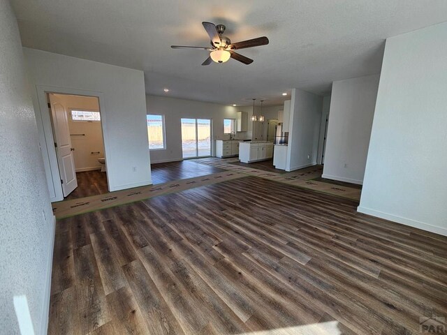 unfurnished living room with dark wood-style floors, ceiling fan, and baseboards