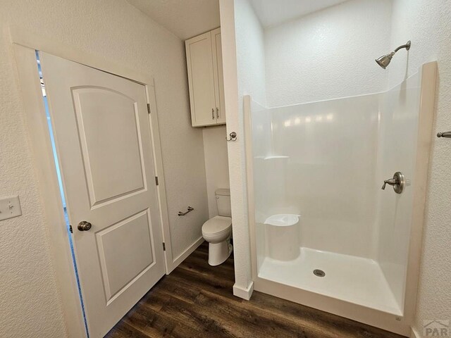 bathroom featuring a stall shower, a textured wall, toilet, and wood finished floors